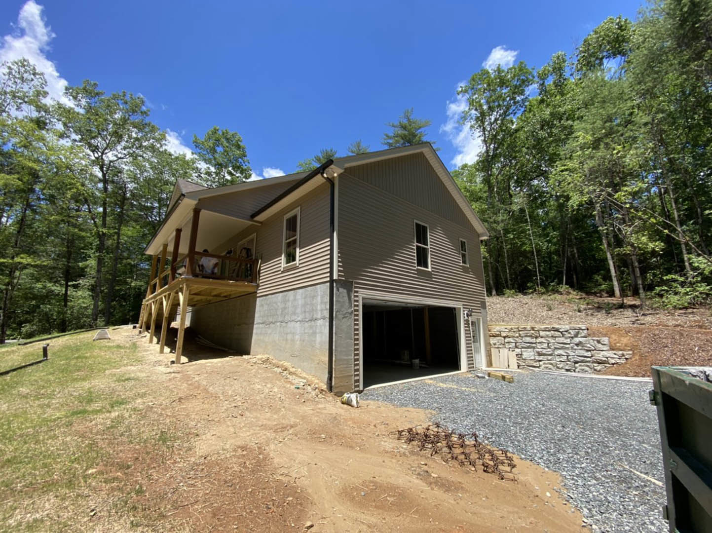 Two-story house with stone and siding exterior, attached garage, concrete driveway, covered front porch, landscaped yard with trees and shrubs