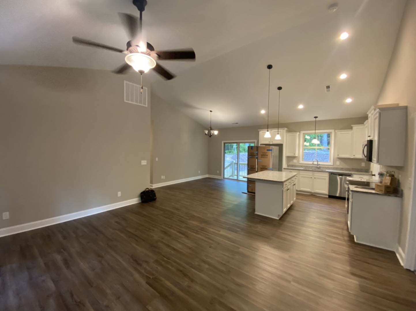 Spacious kitchen with hardwood flooring, white marble-topped island, ceiling fan with light, and a black bag on the floor; window visible in background.