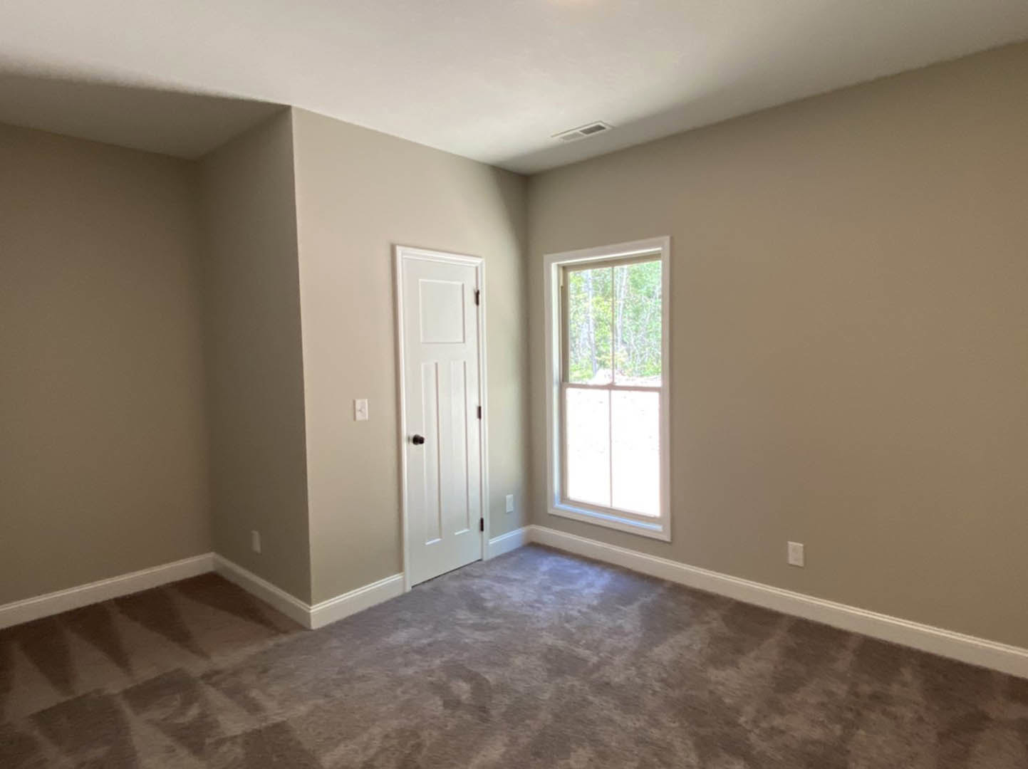 White carpeted room featuring a white door with black knobs, large window overlooking trees, white walls, and ceiling vent