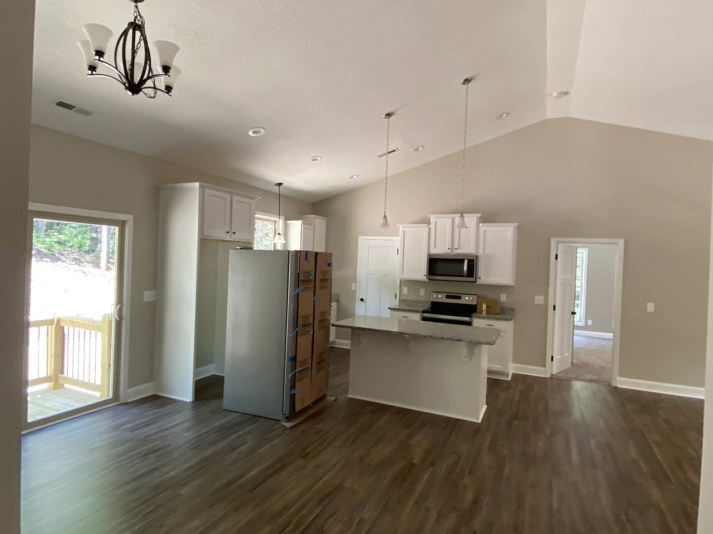 Open kitchen and dining area featuring stainless steel refrigerator, wood flooring, white cabinetry, and modern chandelier.