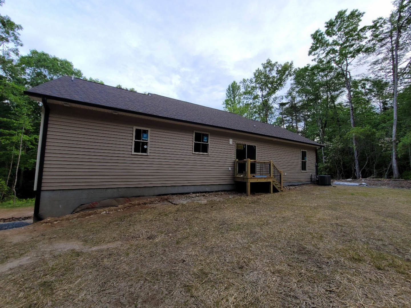 White siding house with covered front porch, wooden deck and railing, grassy yard, large windows, gable roof, mature trees in background.