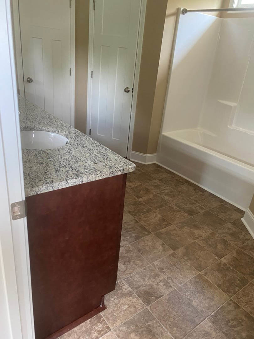 Bathroom with marble countertop, white freestanding bathtub, light tile flooring, and white walls