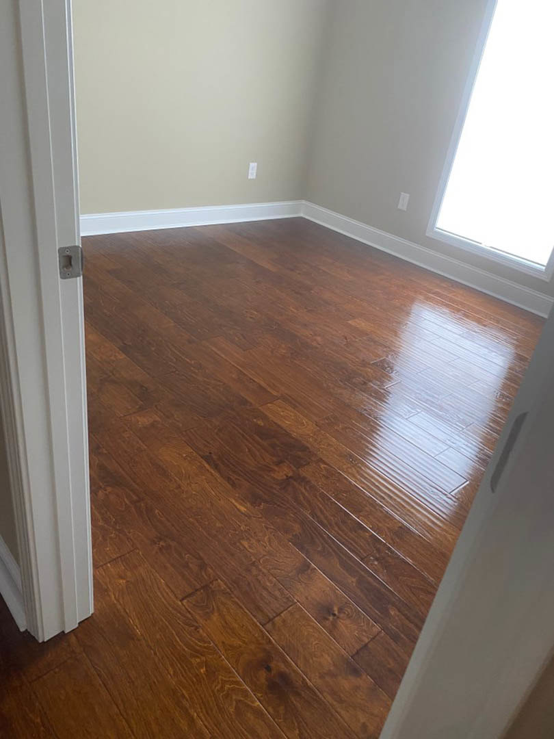 Sunlit room with polished wood floor, large window, white walls, and white door with metal handle