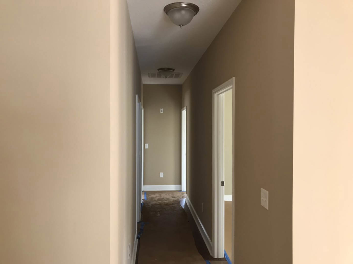 Hallway with beige walls, white trim, carpeted floor, ceiling-mounted light fixture, white electrical outlet, and a close-up of a white door.