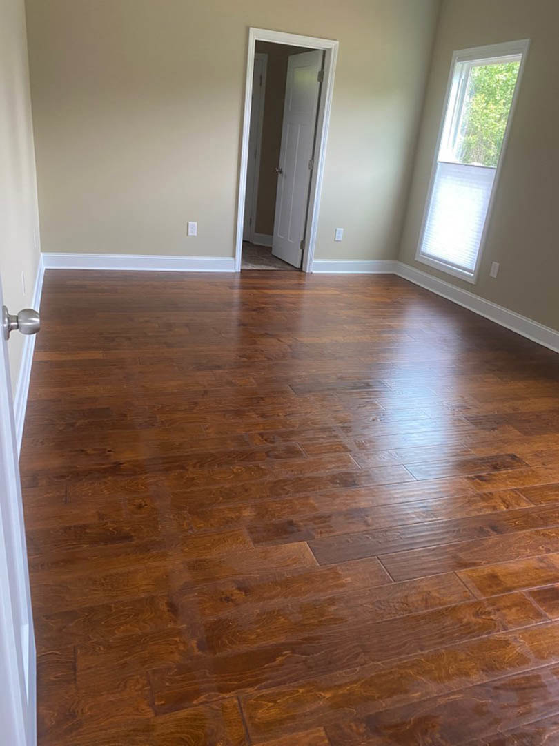 Wood floor room with white walls, white door, window with white shade, and trees visible outside; light switch on wall.
