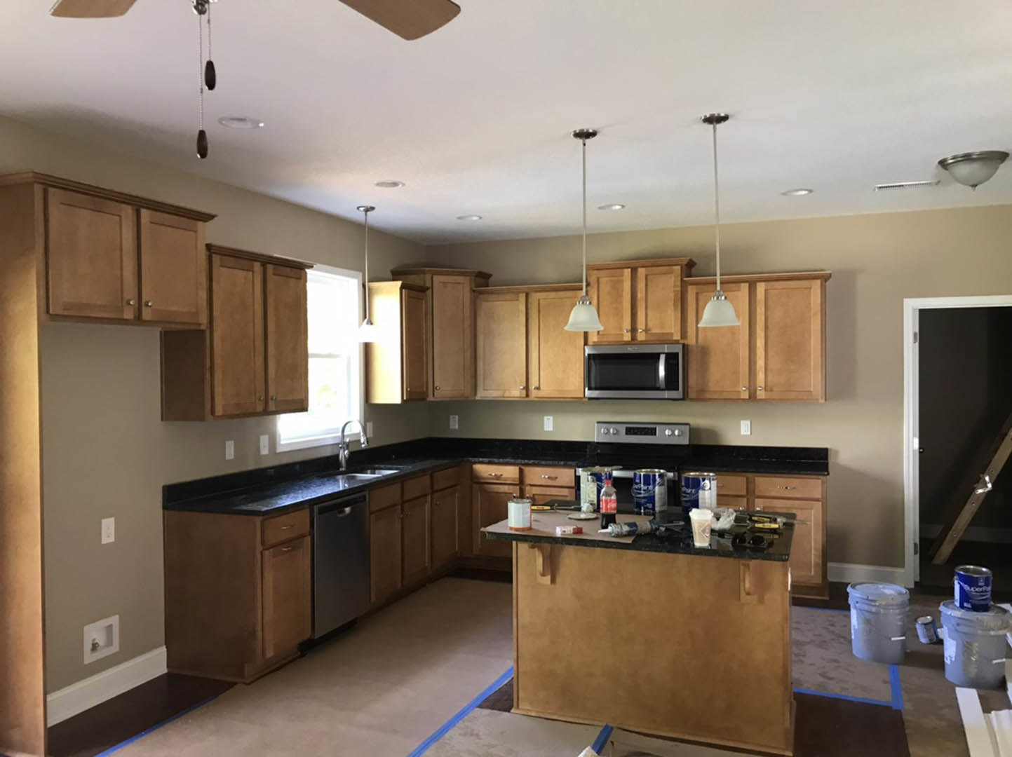 Modern kitchen featuring black countertops, white cabinetry, open microwave door, stainless steel sink, and blue and white can on the counter
