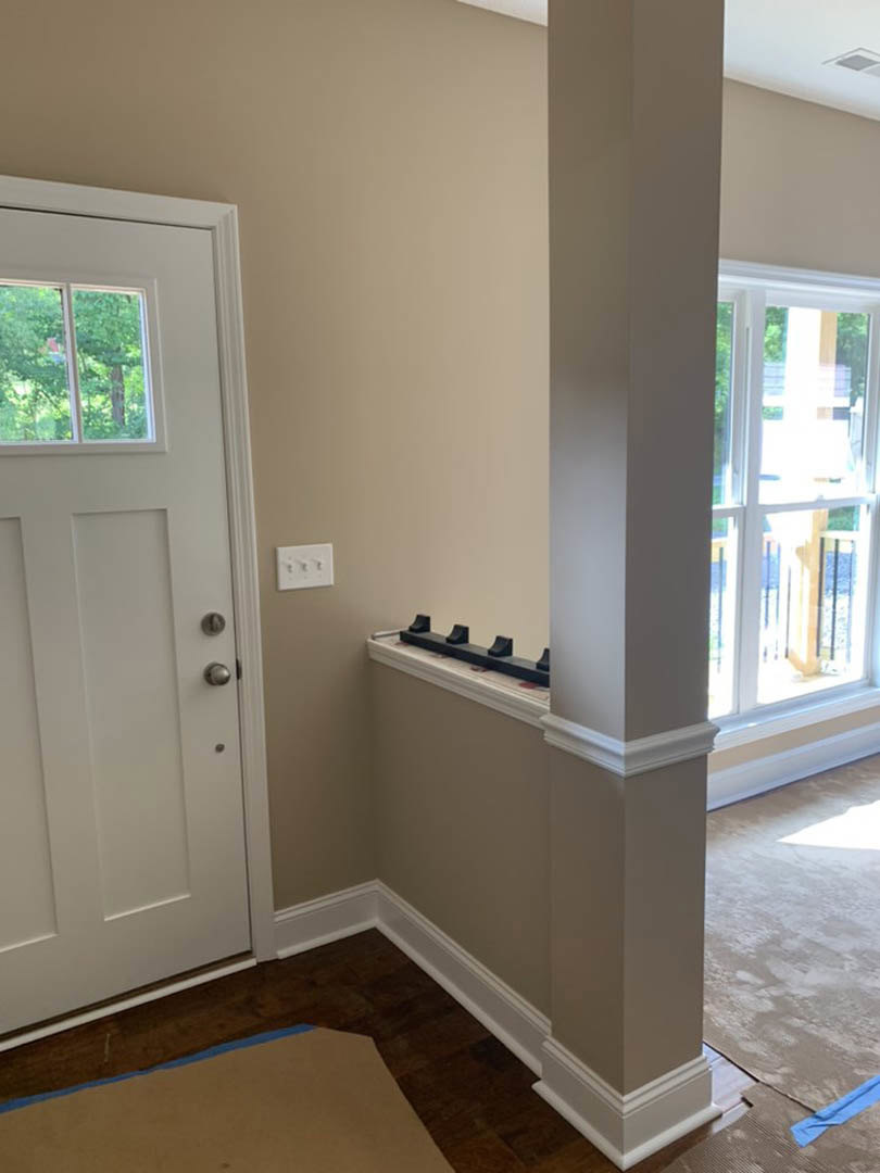 Hallway with light-colored flooring, white walls, white door, window showing trees outside, and light switch on wall
