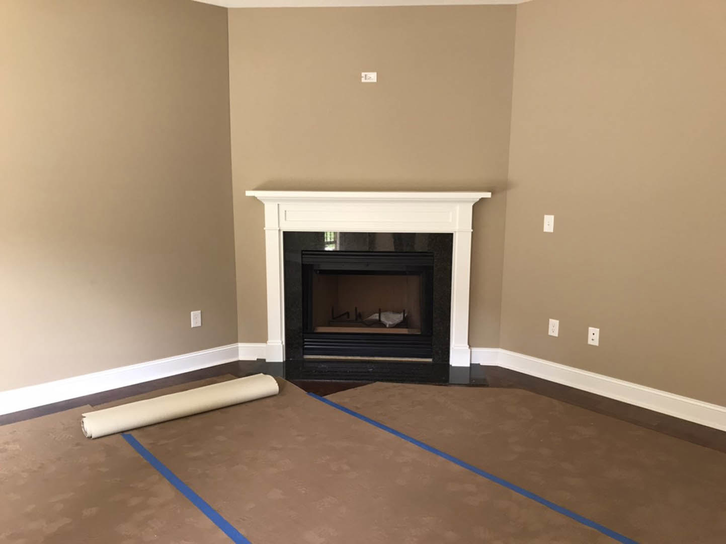 Carpeted living room featuring a white-framed glass fireplace, light switch on the wall, roll of paper and blue tape on a table, laminate flooring near hearth