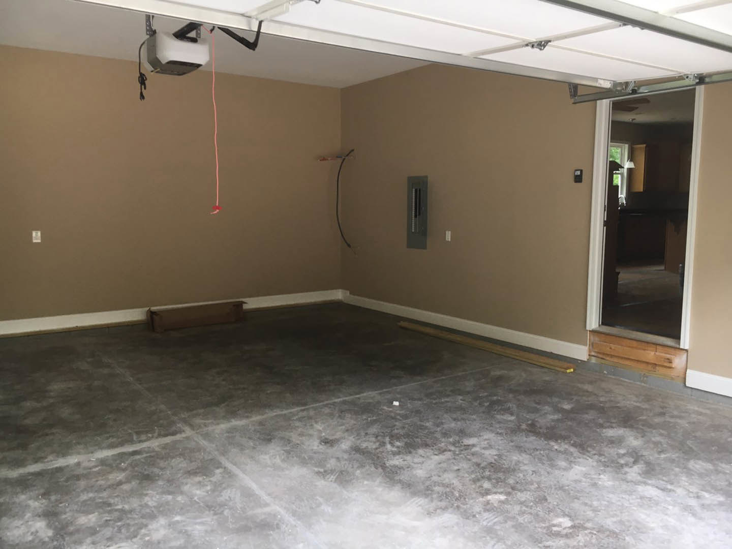 Open garage with concrete floor, white-framed door, white ceiling with border, wood panel detail, and thin pink line along floor.