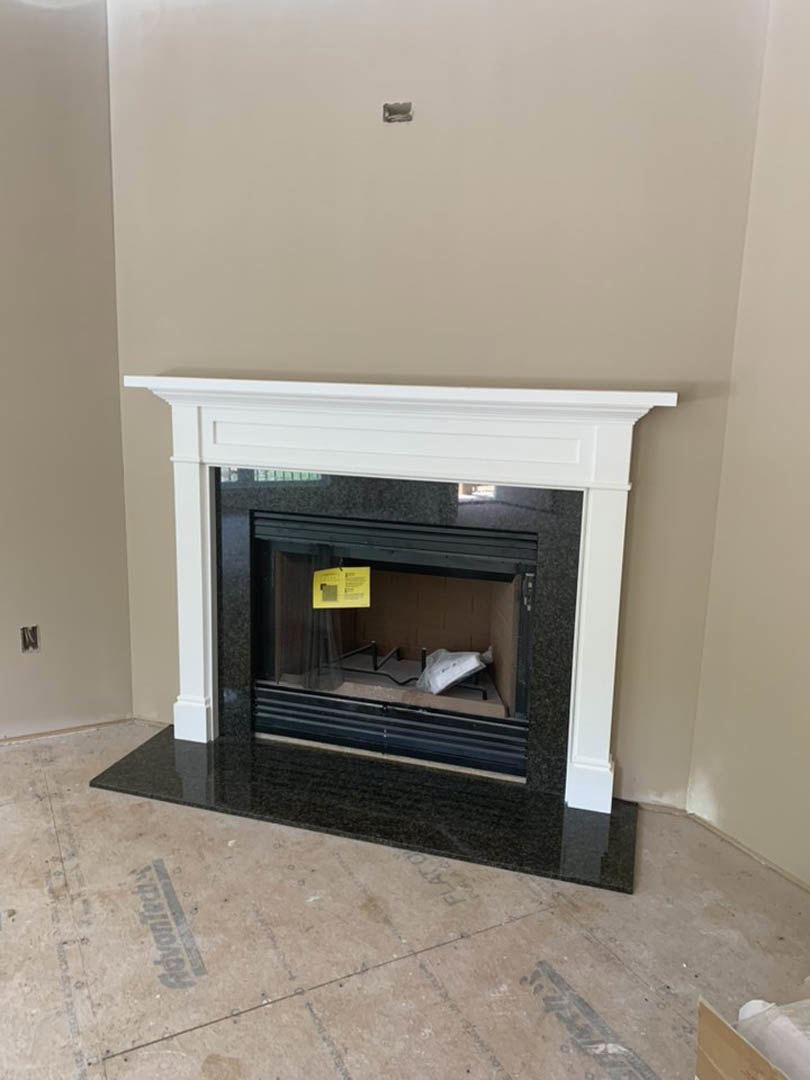 White-framed fireplace with black fire screen set against a light-colored wall, black mat on floor, yellow sign with black text, white decorative object on nearby table