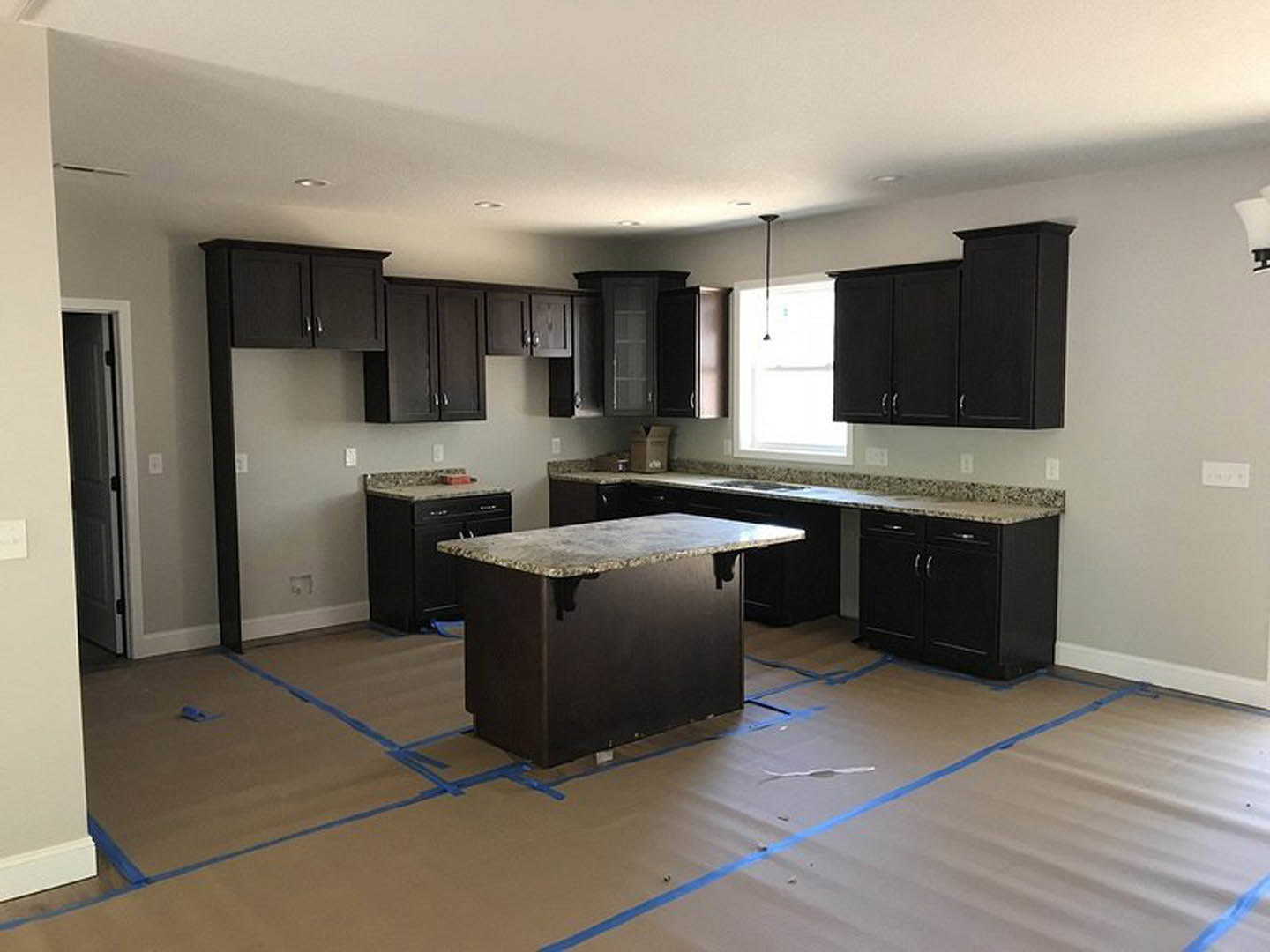 Kitchen with dark wood cabinets, silver handles, marble countertops, stainless steel sink, and white door illuminated by natural light