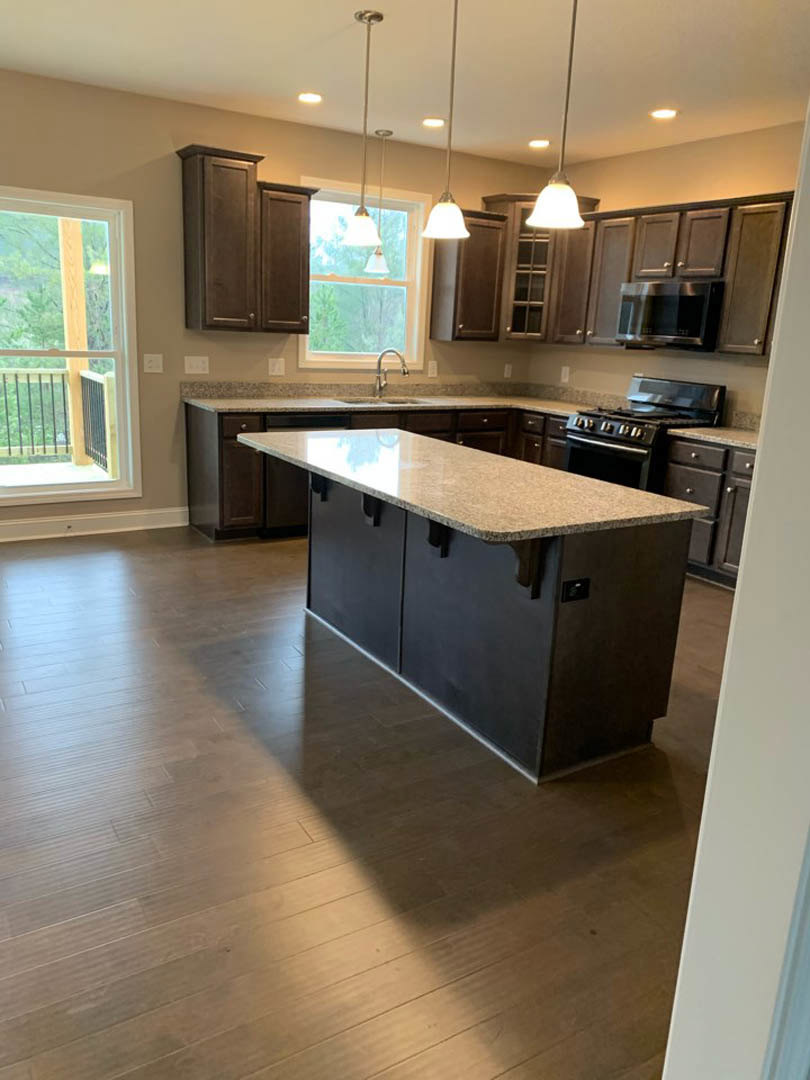 Spacious kitchen featuring a large marble island, wood flooring, white cabinetry, tile backsplash, stainless steel sink, and built-in appliances