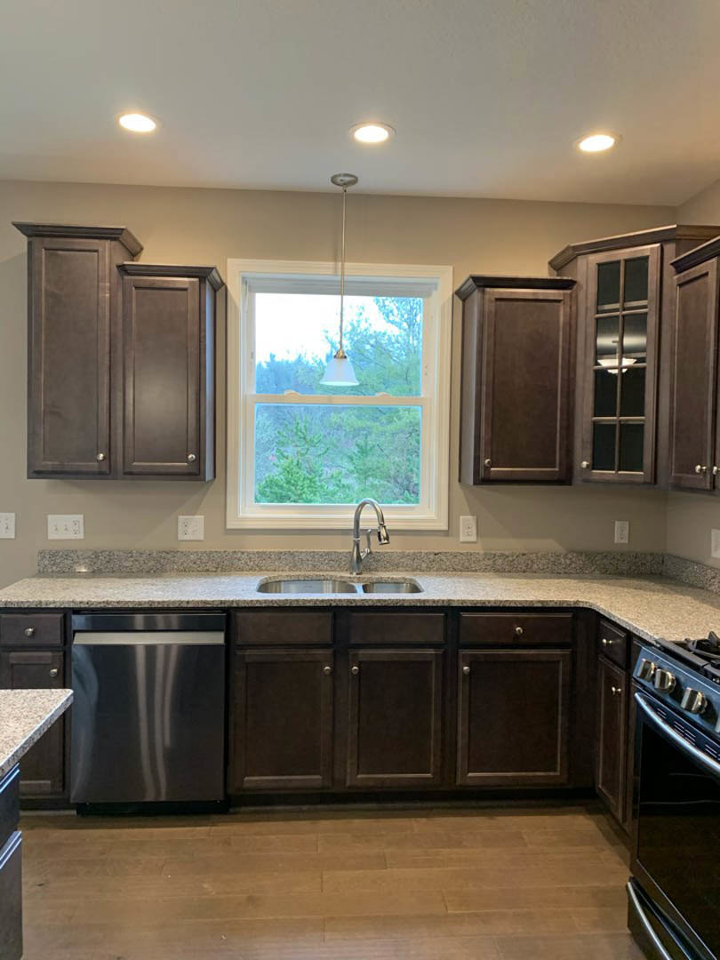 Dark wood kitchen cabinets, stainless steel appliances, stone countertop, large window above sink, modern ceiling light fixture, chrome faucet, metal bar stool at island