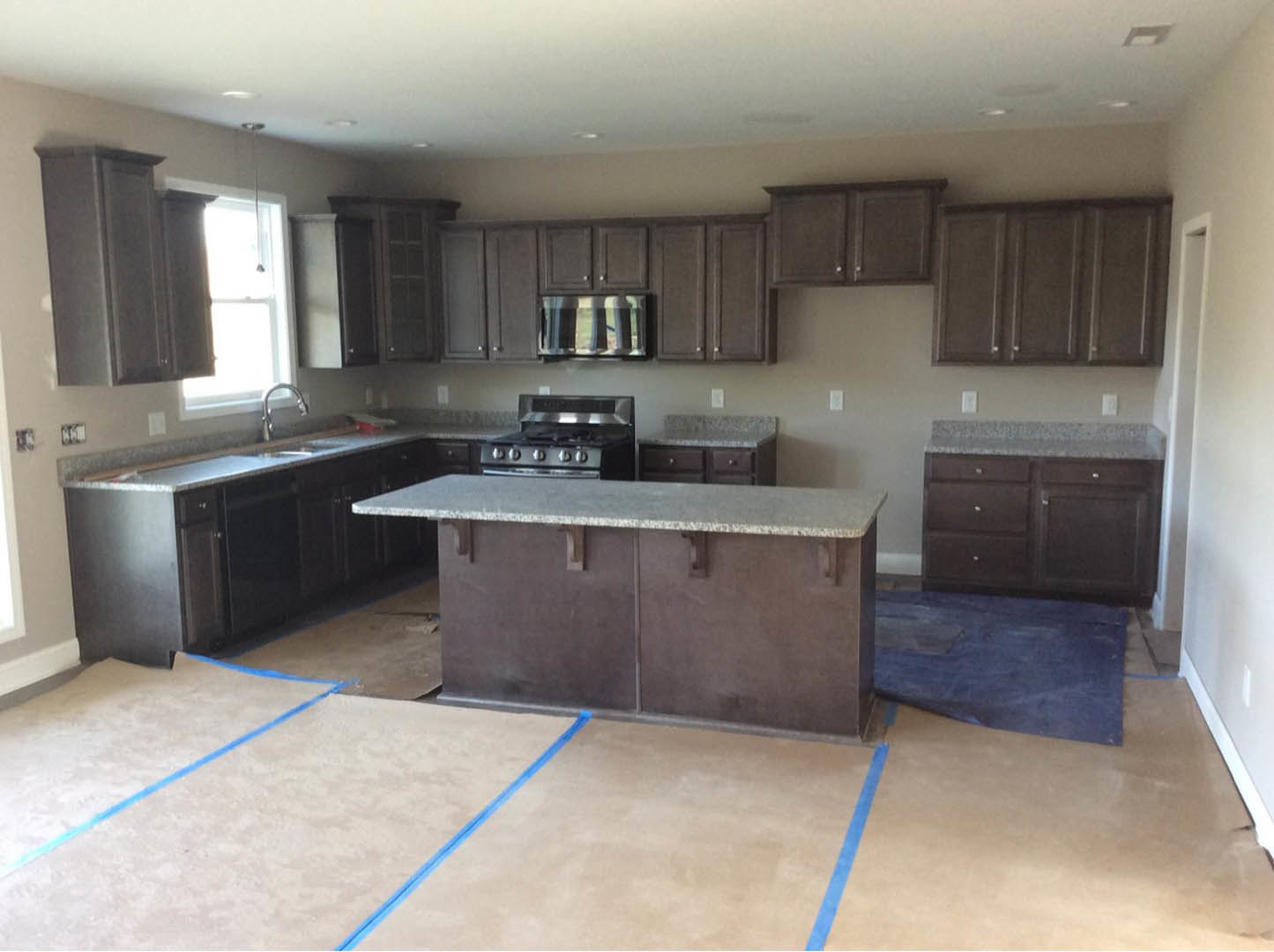 Spacious kitchen featuring a marble-topped island, large window, tile flooring, blue floor mat, stainless steel stove, modern faucet, and white cabinetry
