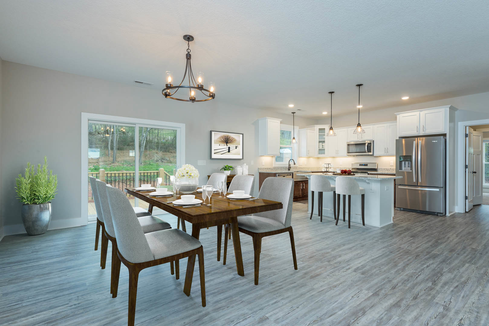 Dining area with wood table and upholstered chairs, open to kitchen featuring stainless refrigerator, white cabinetry, laminate wood flooring, potted plant, and modern chandelier