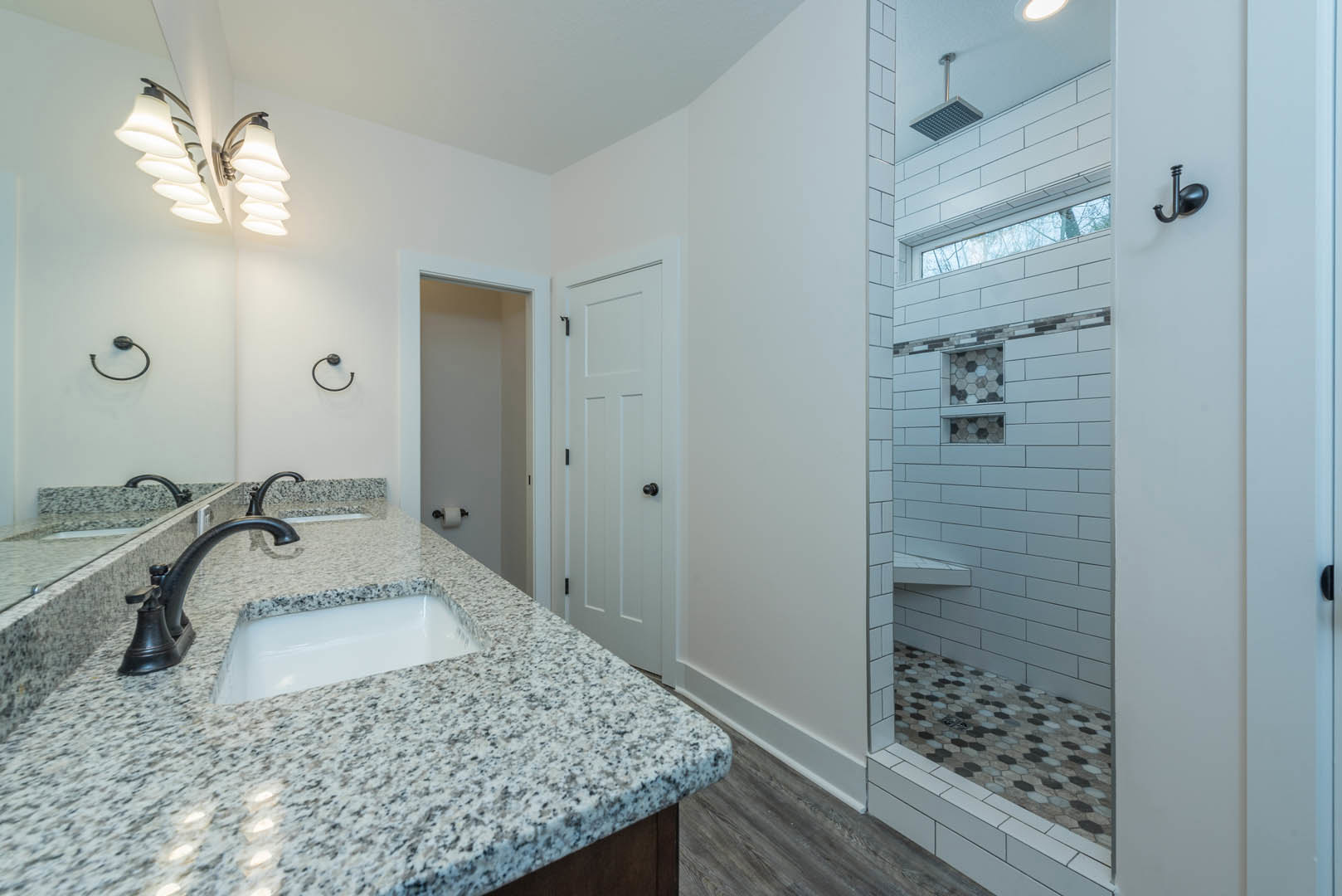 Bathroom featuring a marble countertop with an undermount sink, chrome faucet, glass-enclosed shower with tile floor, and modern light fixture.