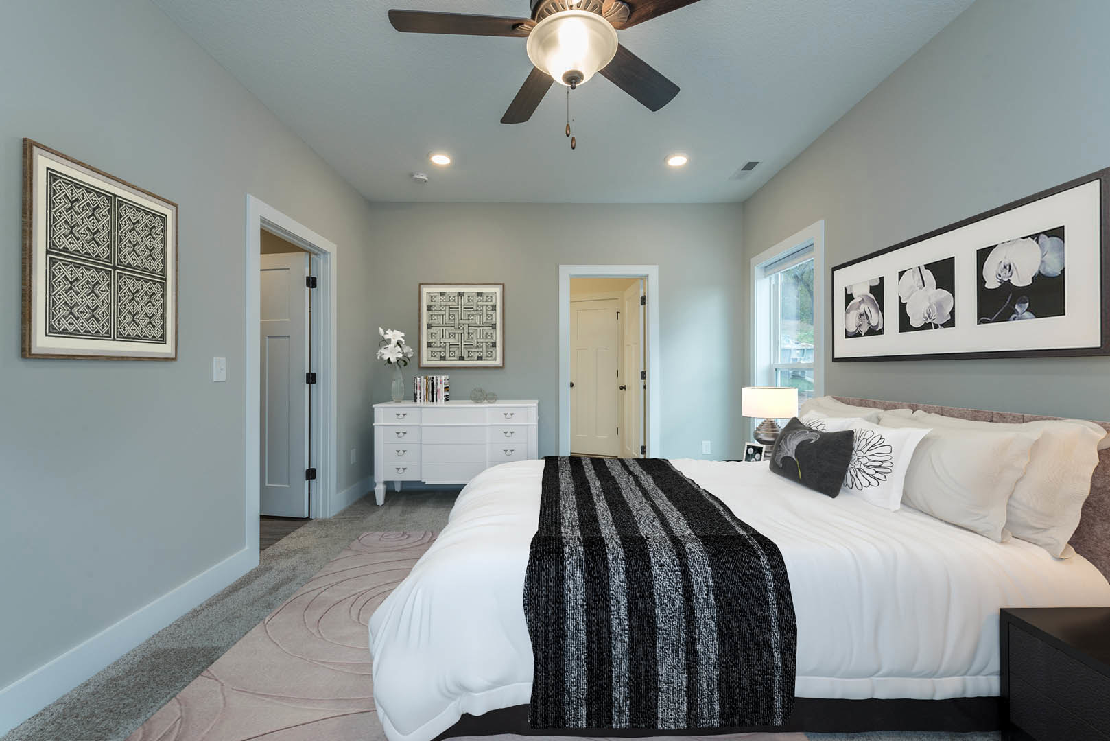 Bedroom with black and white bedding, framed square-pattern artwork on white wall, white door with black knobs, ceiling fan overhead