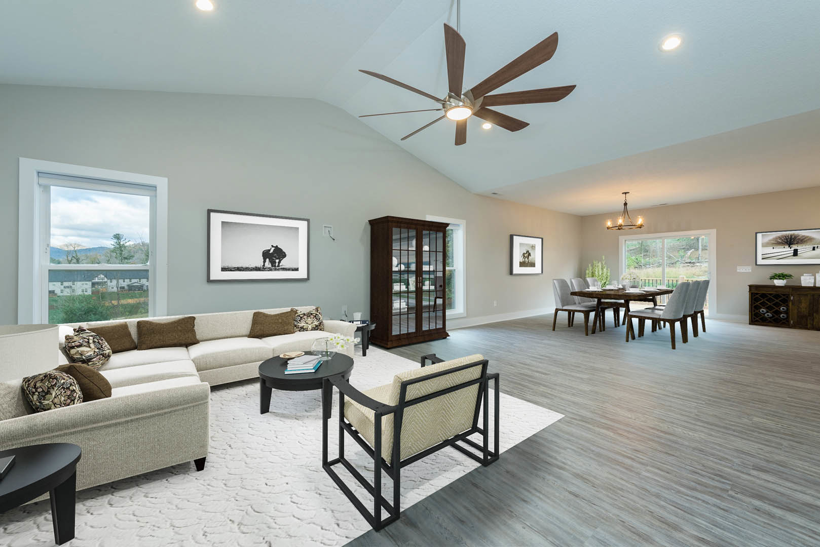 Living room featuring a large ceiling fan with light, spacious table, studio couch, glass cabinet with glass doors, framed horse artwork, and picture frame with person on wall.