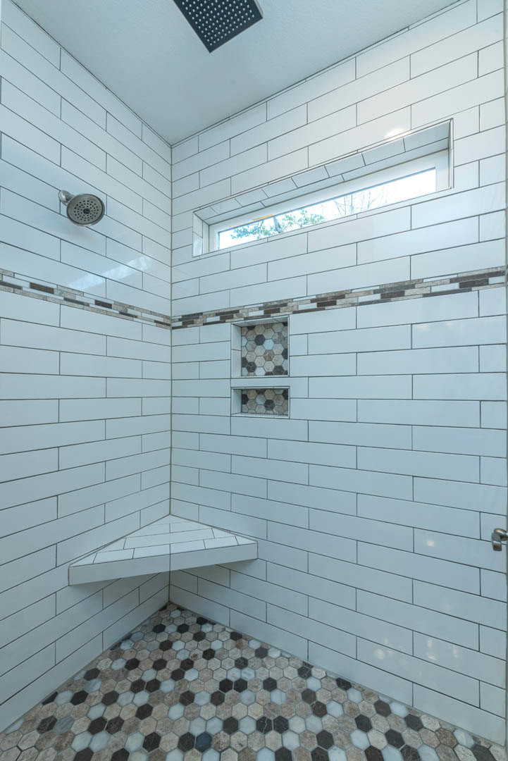 White tile shower with rectangular window, chrome shower head, and black tile floor