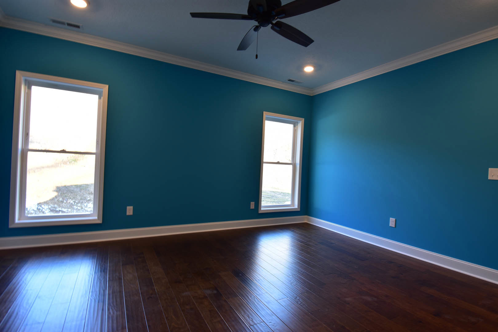 Blue walls, white-framed window, ceiling fan with wood blades, hardwood flooring
