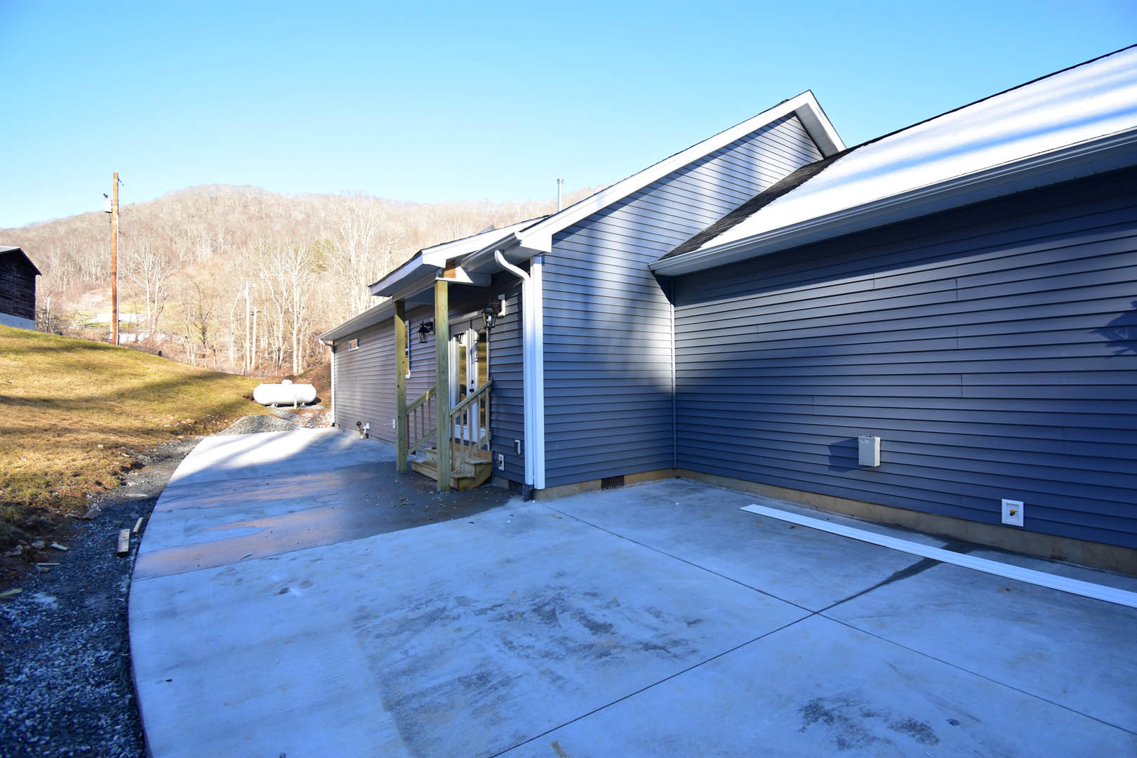 Two-story home with gray siding, concrete driveway, snowy front yard, and bare trees under a clear blue sky