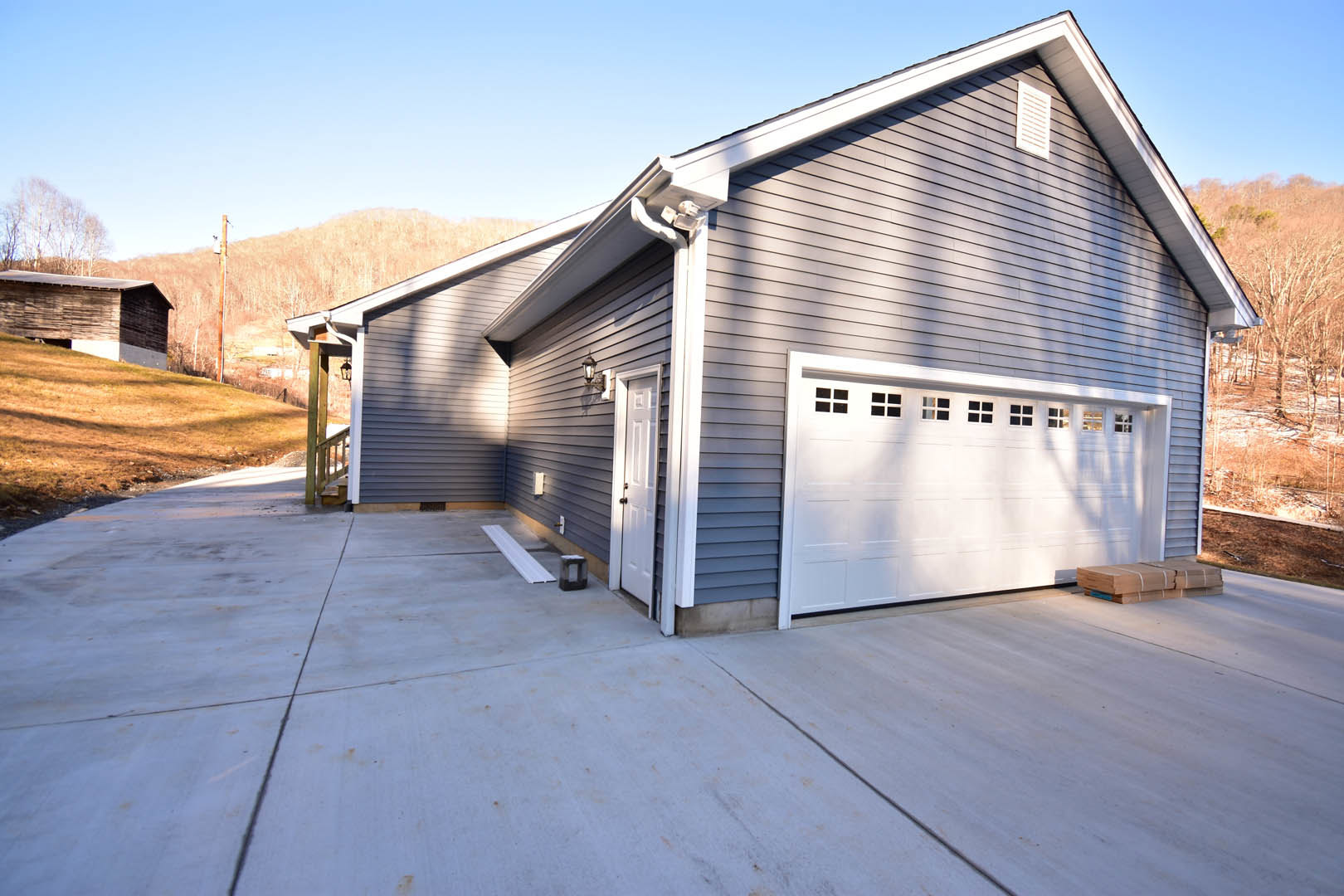 Two-story home with gray siding, white trim, and attached garage featuring windowed doors, concrete driveway, and manicured lawn under blue sky