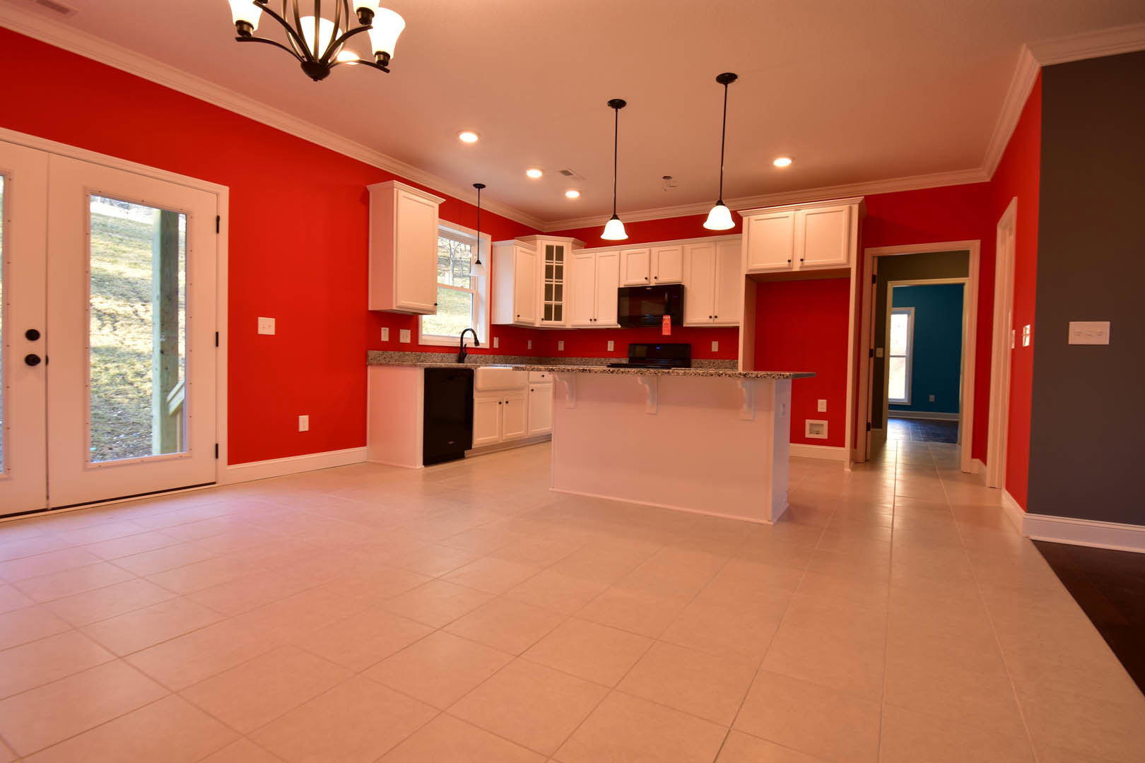 Modern kitchen with a bar seating area, black microwave above white cabinetry, light fixture overhead, pink accent wall, wood beam framing a window, tile flooring, and stone