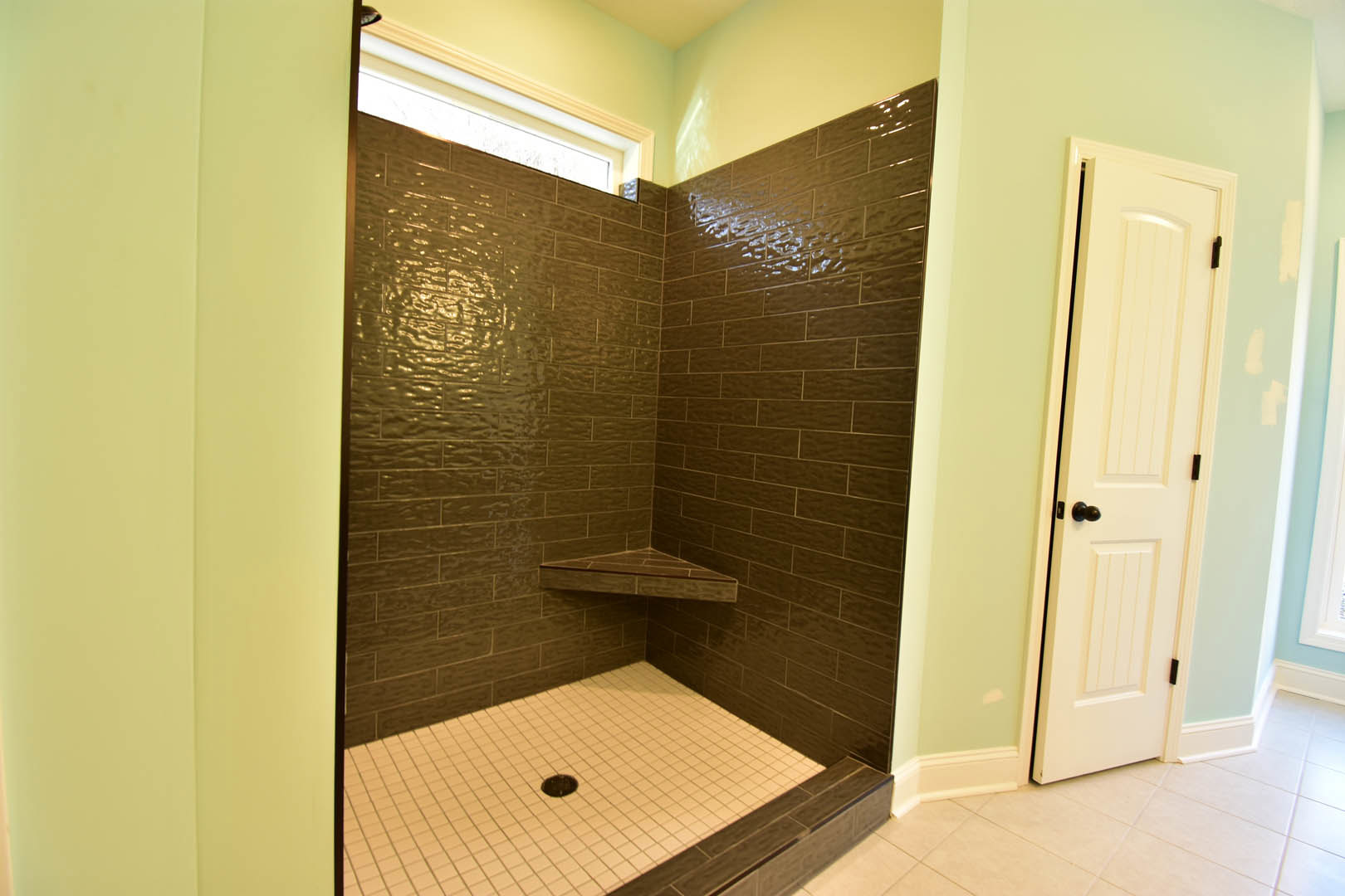 Corner tile shower with glass window, white tile walls, and gray tile floor featuring a central drain