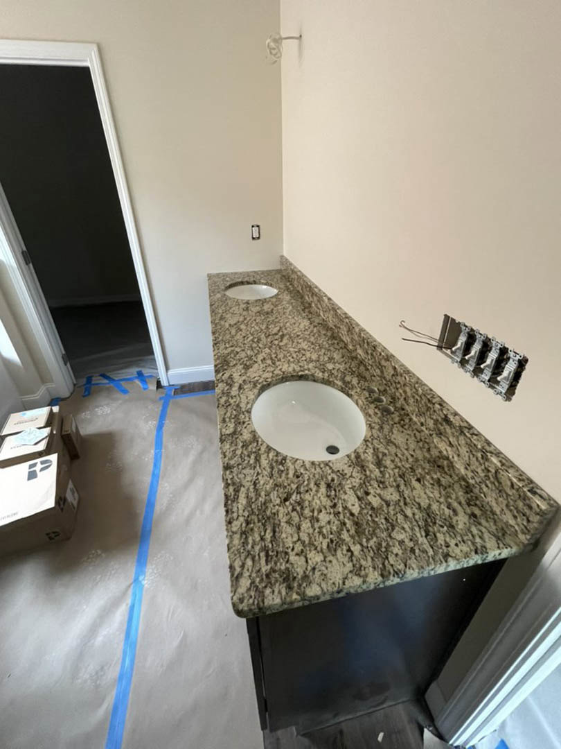 Marble countertop with dual white sinks, large wall mirror, light tile flooring, and black accent wall with white trim in a modern bathroom