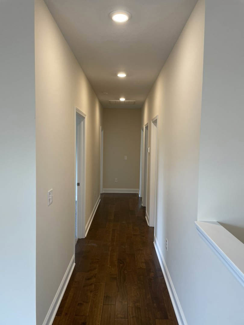 Hallway with white plaster walls, dark wood laminate flooring, white trim, ceiling light fixture, and a blue accent stripe on one wall