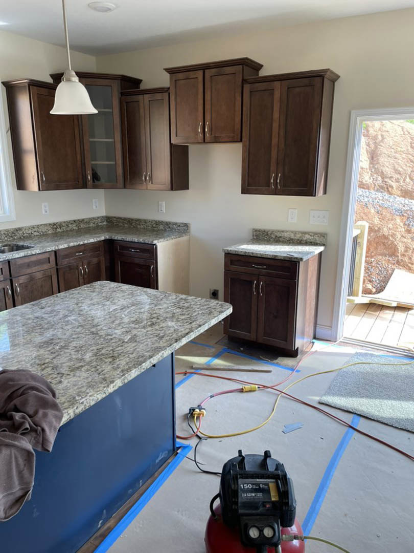 Kitchen featuring dark wood cabinets, blue island with marble countertop, stainless steel appliances, and window set in a stone accent wall
