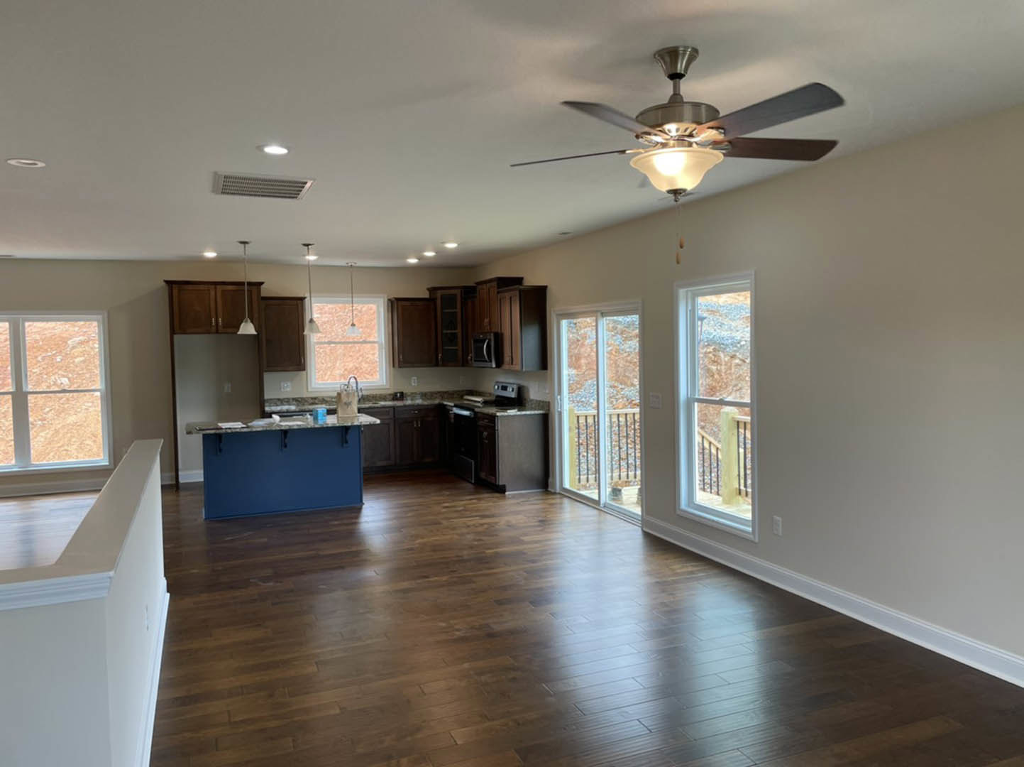 Open kitchen with blue island featuring marble countertop, ceiling fan with light fixture, hardwood flooring, large window with exterior railing visible.