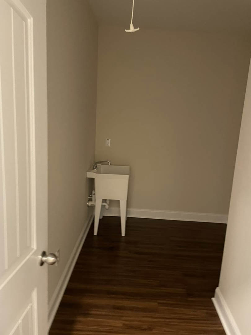 White porcelain sink with chrome faucet set against a white paneled door, wood flooring with white baseboards, soft natural light, minimalist bathroom design.