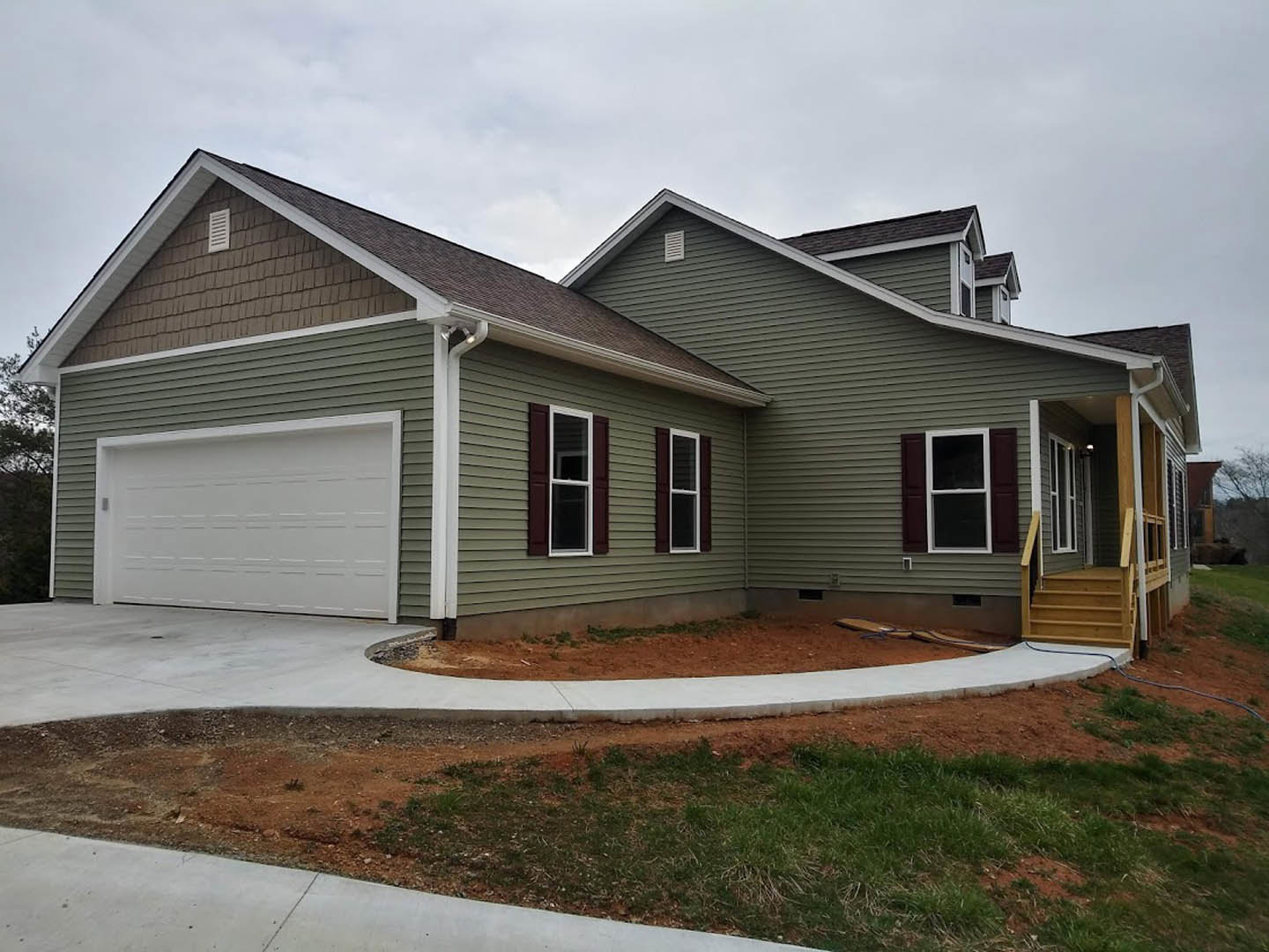Two-story home with light siding, white-framed windows, white front door, attached garage with paneled door, wooden porch steps, concrete driveway, and grassy yard.