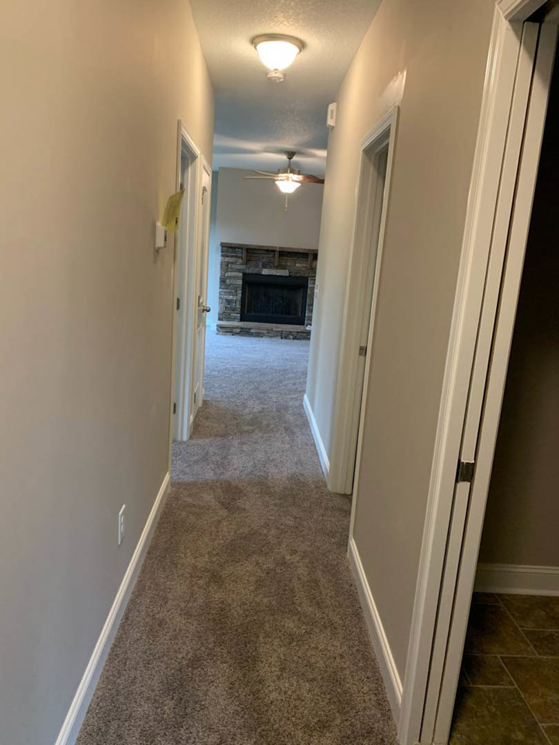 Hallway with carpeted walls, white trim, stone fireplace, ceiling light fixture, window, and tile flooring