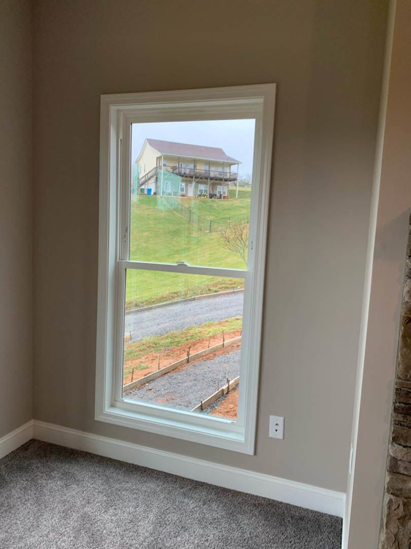 Large window set in a painted wall, overlooking green grass and a neighboring house, with carpeted floor visible inside the room