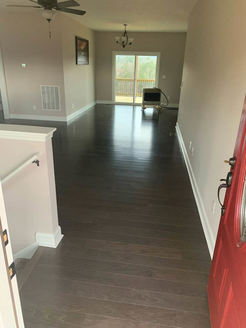 Hallway with dark wood floors, red entry door, sliding glass door with screen, white walls, and modern chandelier