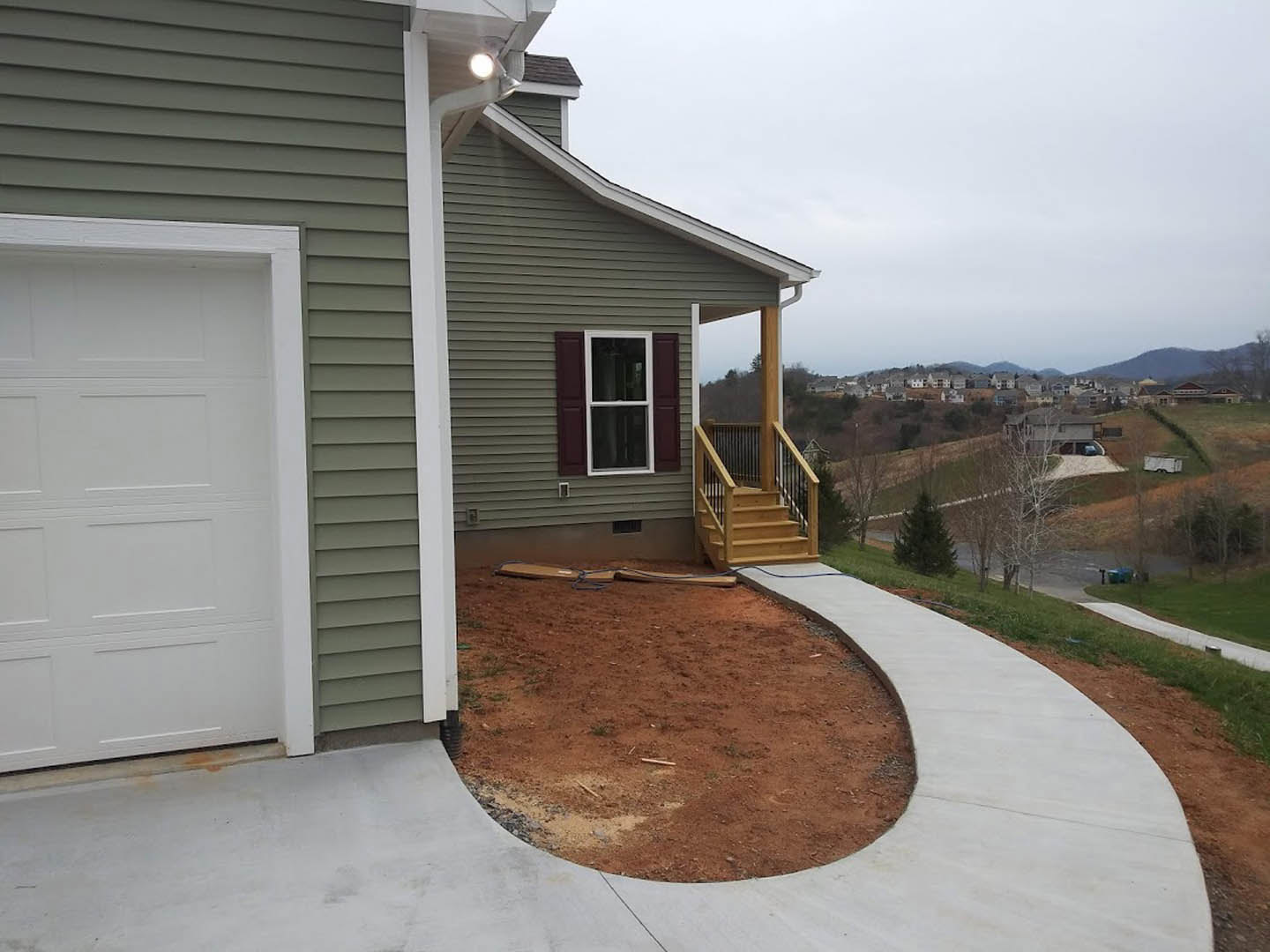 Two-story home with white siding, wooden porch railing, white-framed windows, concrete driveway and walkway, white garage door, green-leafed tree in front yard