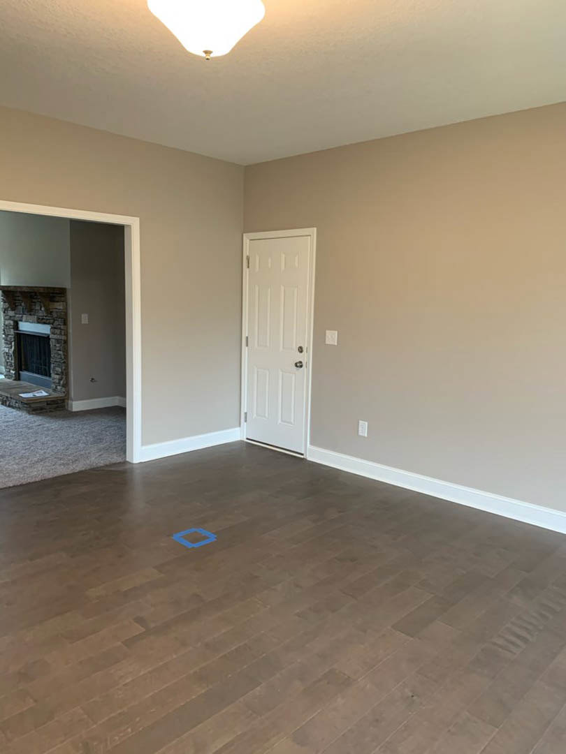 White paneled door with silver knobs, light wood flooring, stone fireplace, modern light fixture, blue accent rug, and beige carpet in a residential interior.