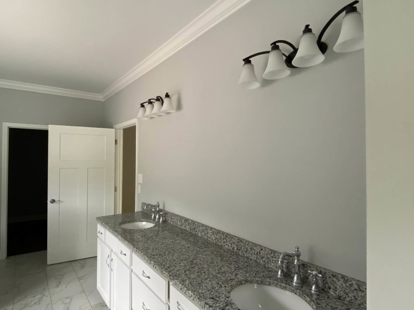 Bathroom with marble countertops, white cabinets, three-lamp light fixture, white door with silver handle, close-up of sink and faucet, black screen with white border