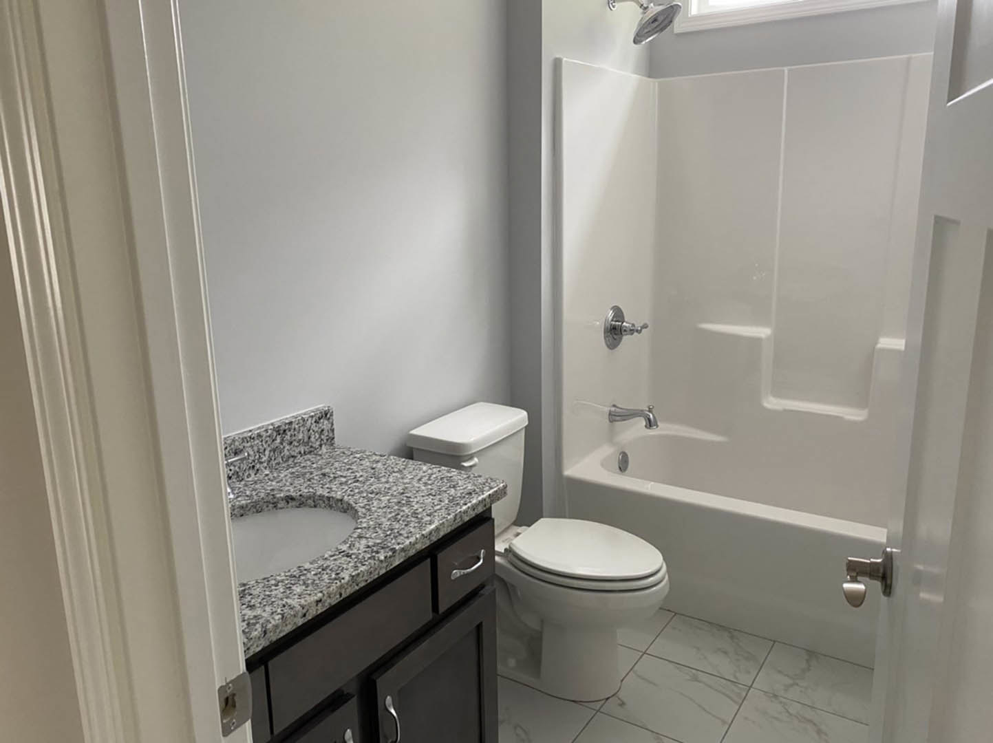 Modern bathroom featuring white ceramic sink with chrome faucet, closed white toilet, glass-enclosed shower with chrome showerhead, large wall mirror, and light gray tile walls and