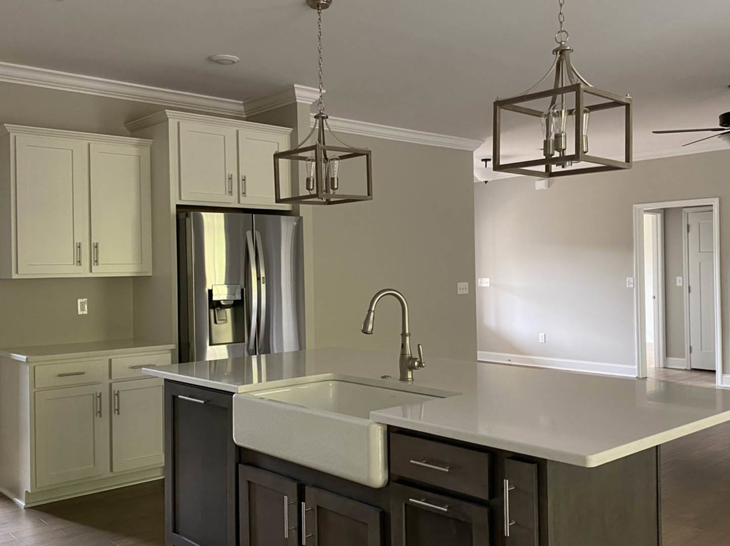 Modern kitchen with stainless steel refrigerator, undermount sink with chrome faucet, white cabinetry, quartz countertops, pendant light fixture, and white door with nearby light