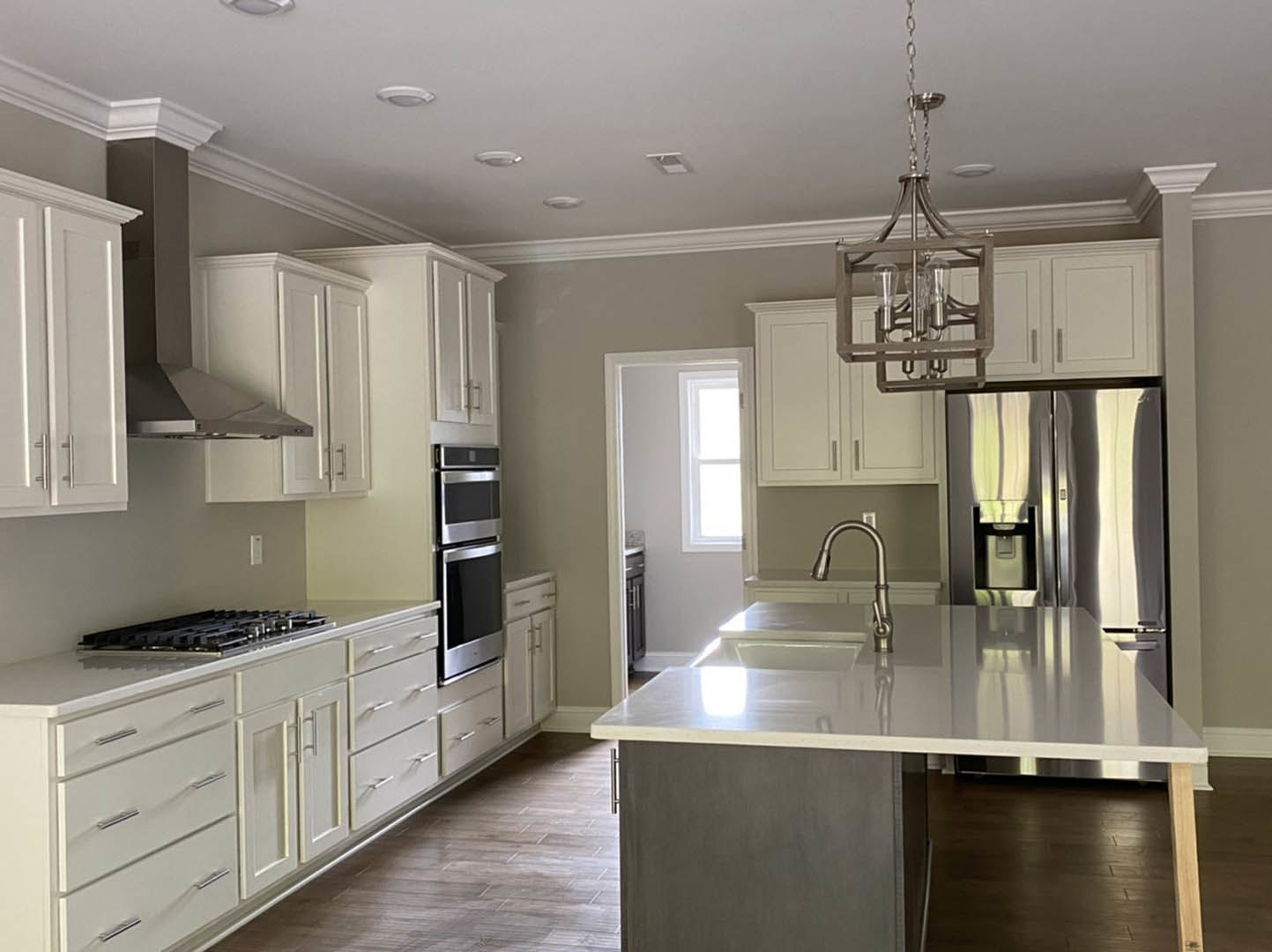 White kitchen with shaker cabinets, stainless steel refrigerator with water dispenser, built-in microwave, large central island, quartz countertops, undermount sink with chrome