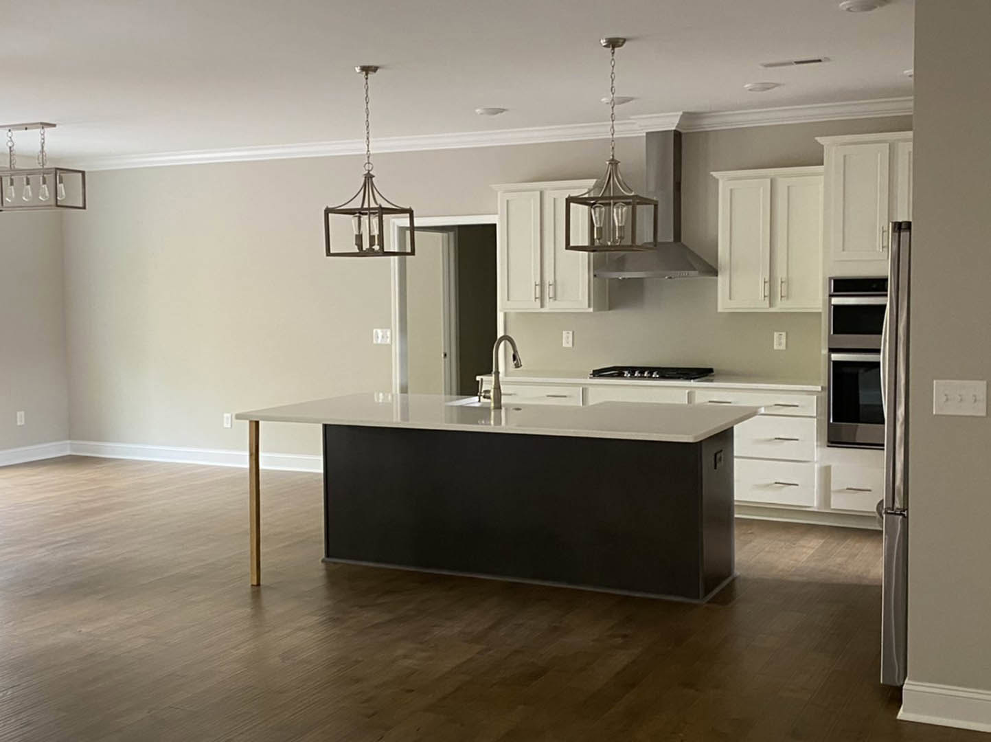 Black and white kitchen island with built-in stove, wood flooring, black accent wall, white cabinetry, modern chandelier, and stainless steel sink