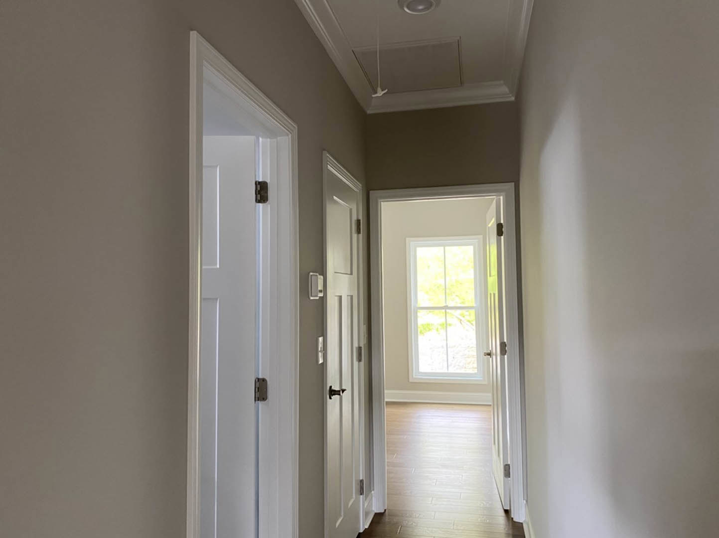 Hallway with white paneled doors, white trim, and a window with a white frame letting in natural light onto light-colored flooring