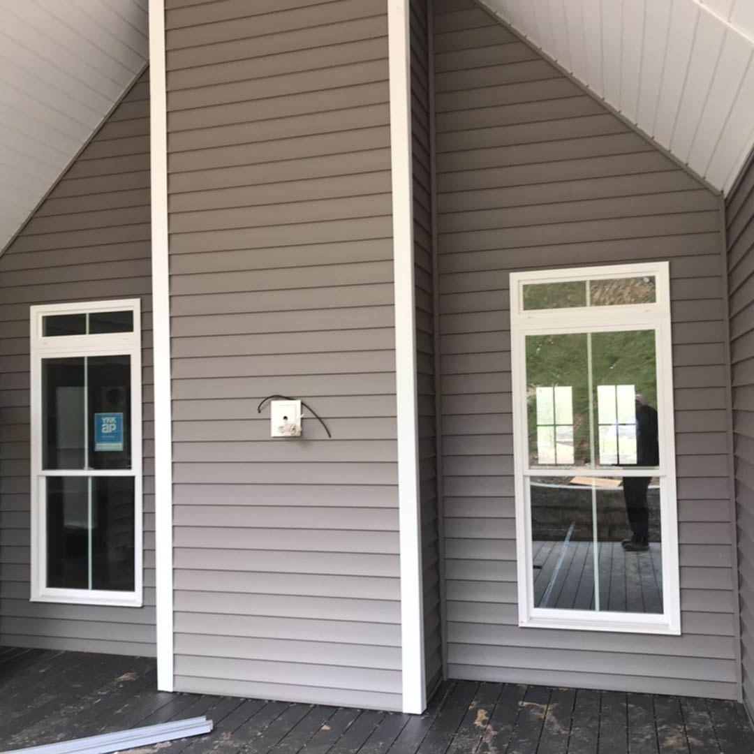 Two-story home with white roof, light-colored siding, covered porch, multiple sash windows, and a white electrical outlet with black wire visible on exterior wall