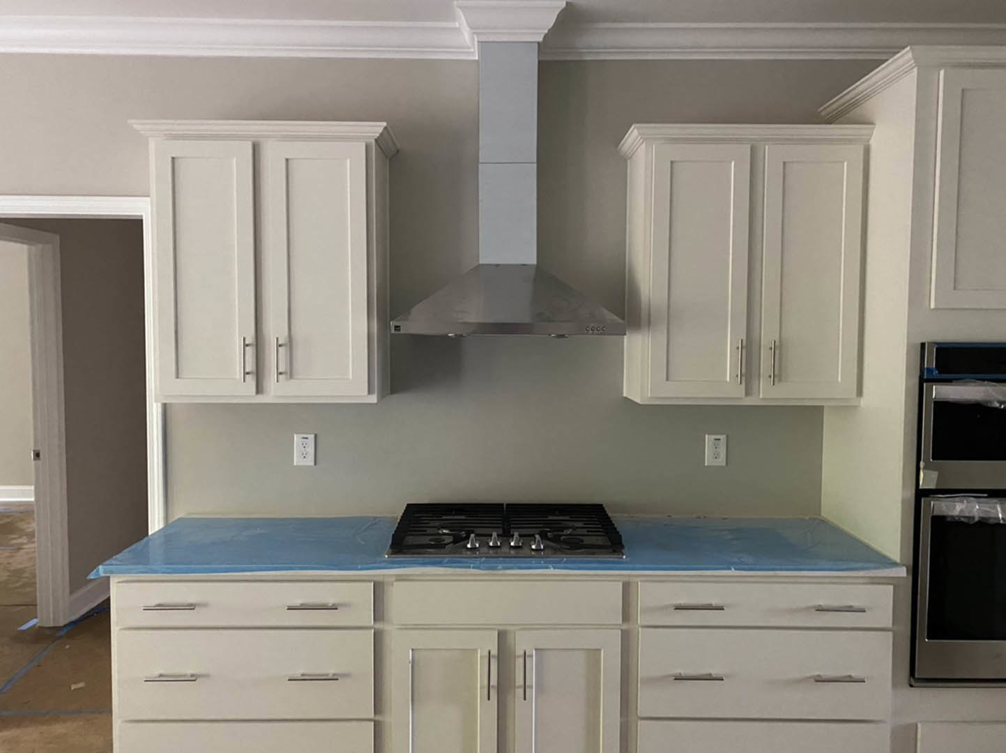 White kitchen cabinets with silver handles, blue countertops, stove top covered in blue plastic wrap, plastic bag hanging on refrigerator door, close-up of cabinet knob.