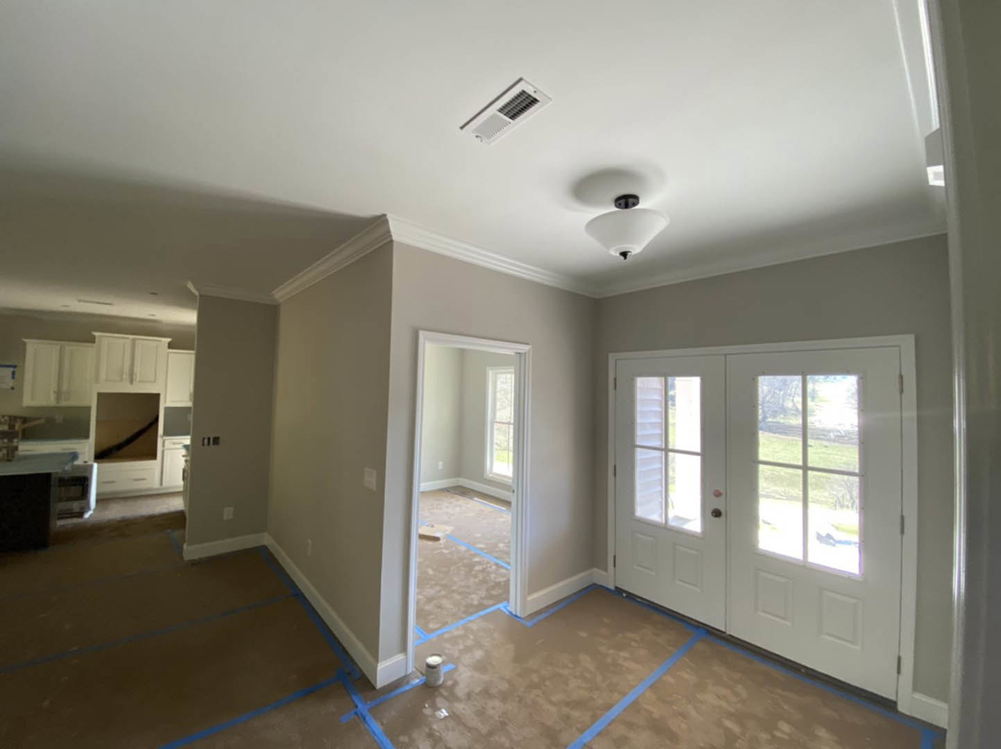 Room with double white doors featuring glass panes, blue painter’s tape on door edges, laminate wood flooring, ceiling vent, recessed white light fixture, paint can on floor, and