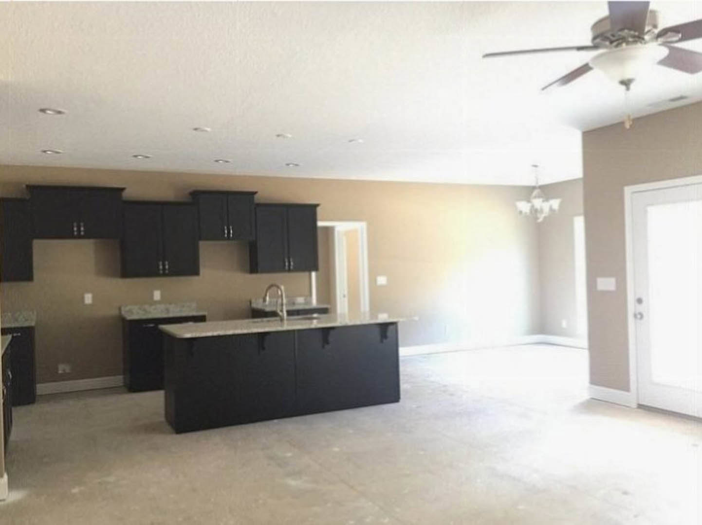 Modern kitchen featuring black cabinets above a white wall, black countertop with integrated sink, white door in the background, and ceiling fan with light fixture.