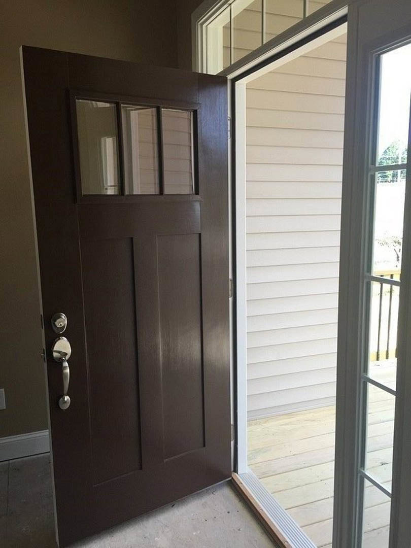 White paneled door with rectangular glass panes, silver handle, white railing, and adjacent light-colored wooden floor